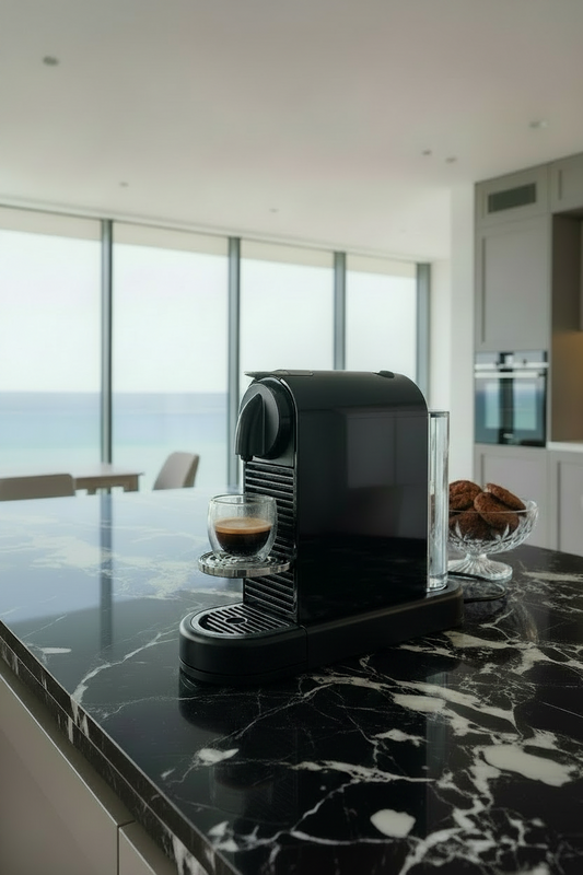 A black Nespresso CitiZ coffee machine on a table with a glass cup of espresso underneath.
