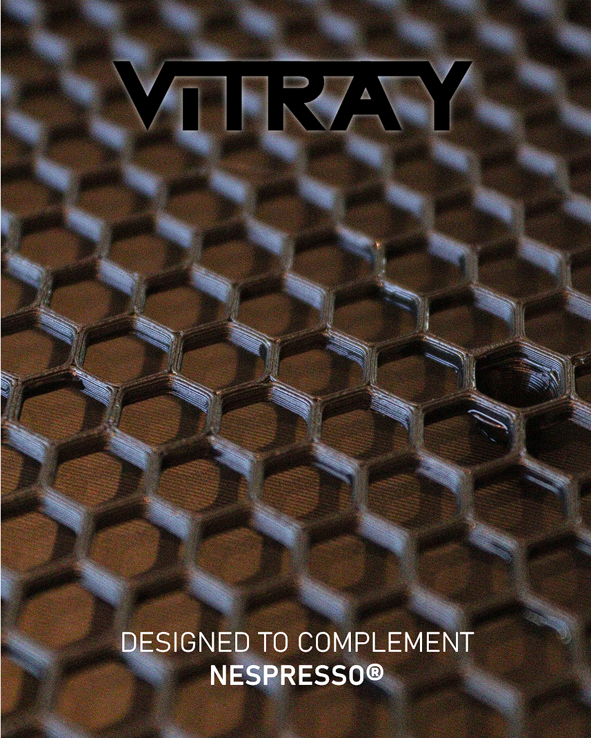 A close-up promotional graphic showing a honeycomb-style metallic mesh surface with the brand name VITRAY at the top and the text 'DESIGNED TO COMPLEMENT NESPRESSO®' at the bottom.